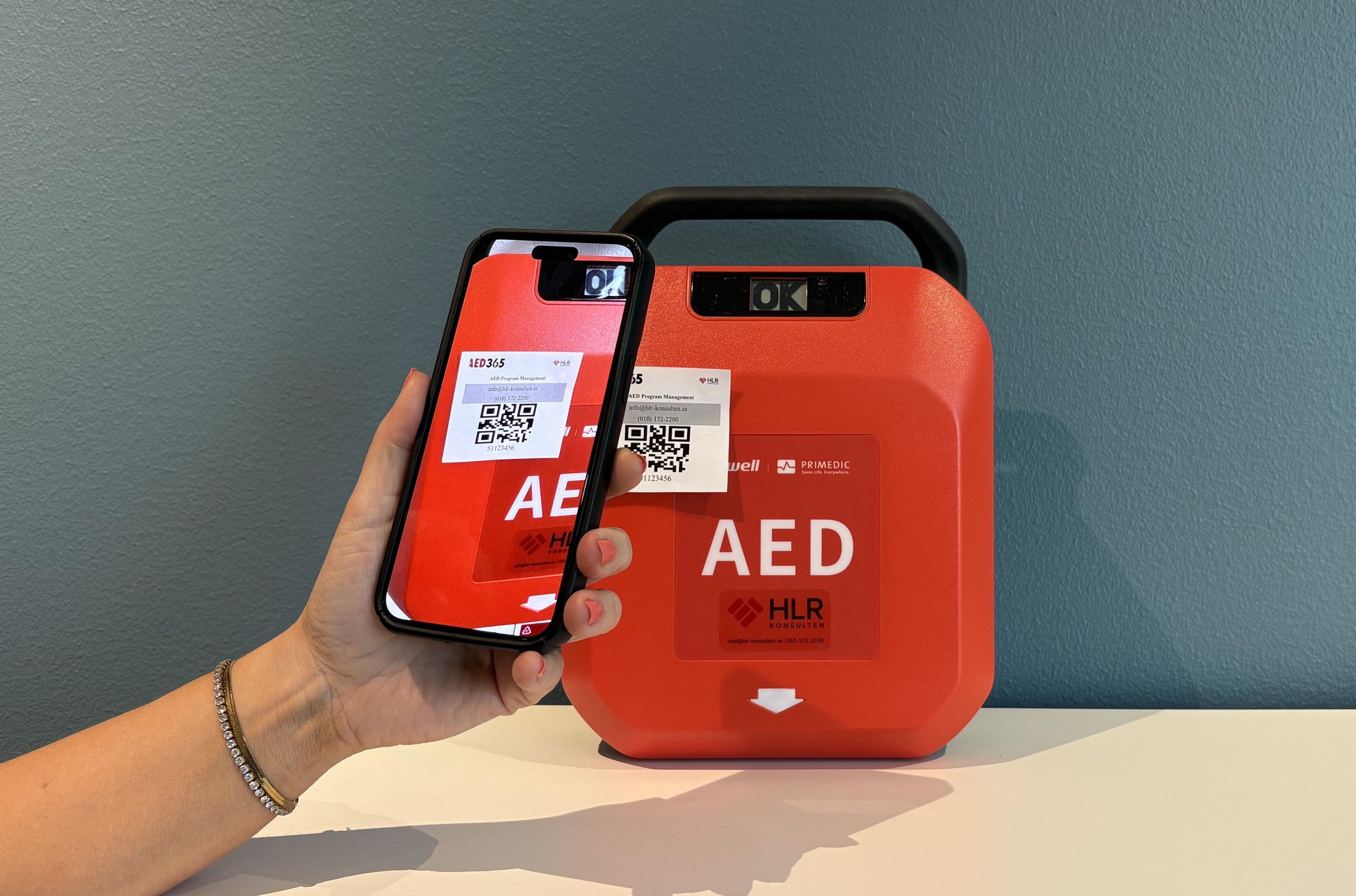 Hand med mobiltelefon som skannar hjärtstartare med hjälp av AED365